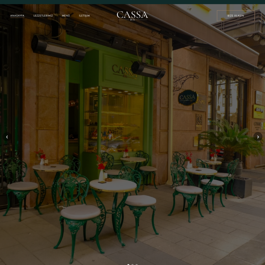 Outdoor cafe seating with green wrought iron chairs and white tabletops along a storefront